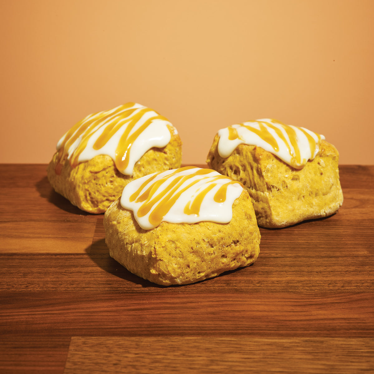 Three fresh pumpkin scones arranged on a dark wooden bakery countertop