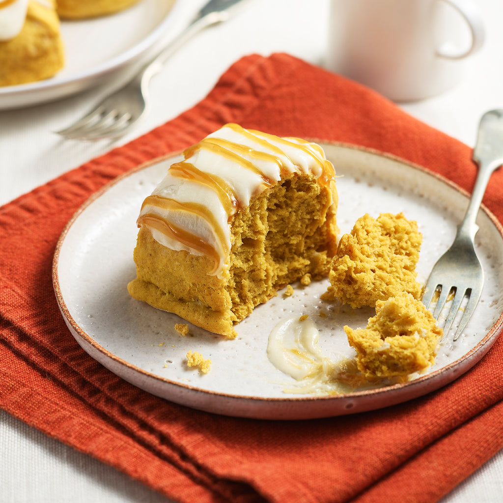 A pumpkin spice scone split open on a plate to show the soft texture, cream cheese glaze, and caramel drizzle